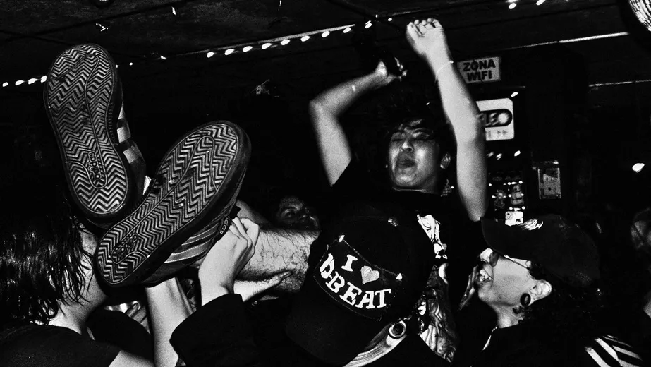 Público con los brazos en alto frente al escenario, en blanco y negro.